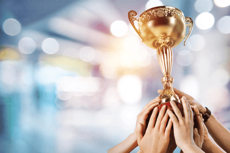 Several hands lift up a gold award trophy