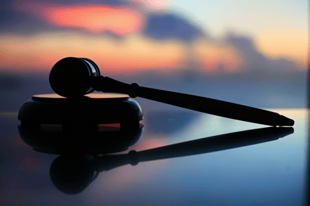 silhouetted by a sunset, a gavel lays upon a reflective surface 