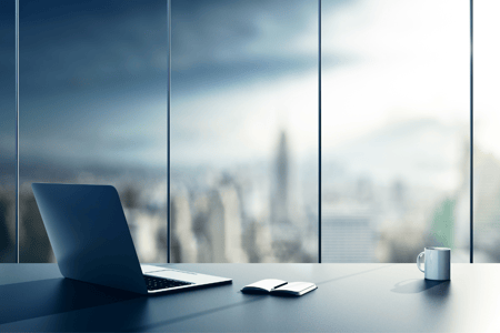 laptop, notepad and coffee mug on desk with city scape in the background
